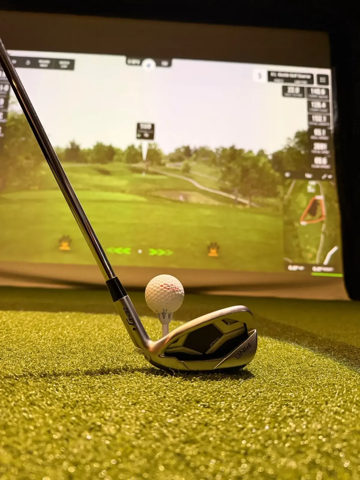 Close-up of a golf club head at address in front of the simulator screen